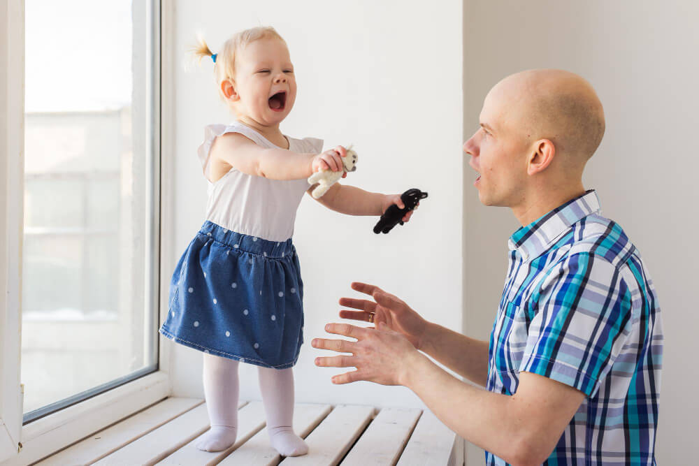 Enfant de 18 mois riant, la main levée, après avoir tapé gentiment son parent.