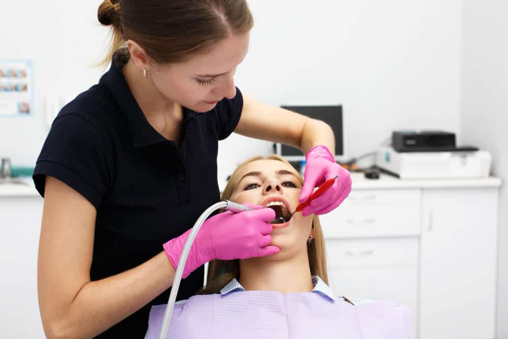 Dentiste effectuant un polissage et une application de fluor (prophylaxie) sur les dents d'un patient.