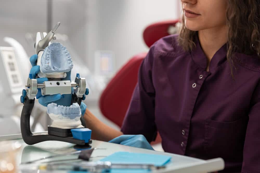 Technicien prothésiste dentaire travaillant sur un dentier en cire dans son laboratoire.