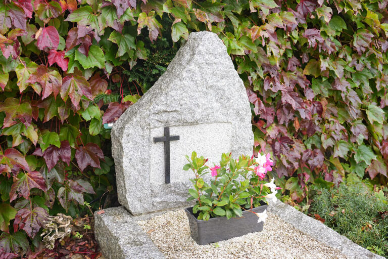 Un monument funéraire en granit gris fleuri avec soin dans un cimetière paisible pour illustrer le lieu de recueillement après une inhumation.