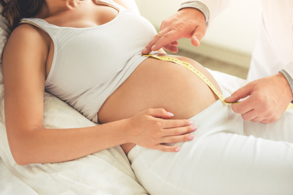 Une sage-femme mesurant le ventre d'une femme enceinte lors d'une consultation de fin de grossesse.