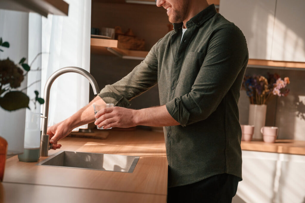 Comment faire analyser l’eau de votre robinet gratuitement ? 2 Un particulier remplissant un flacon en verre directement au robinet de sa cuisine pour un test de pureté.