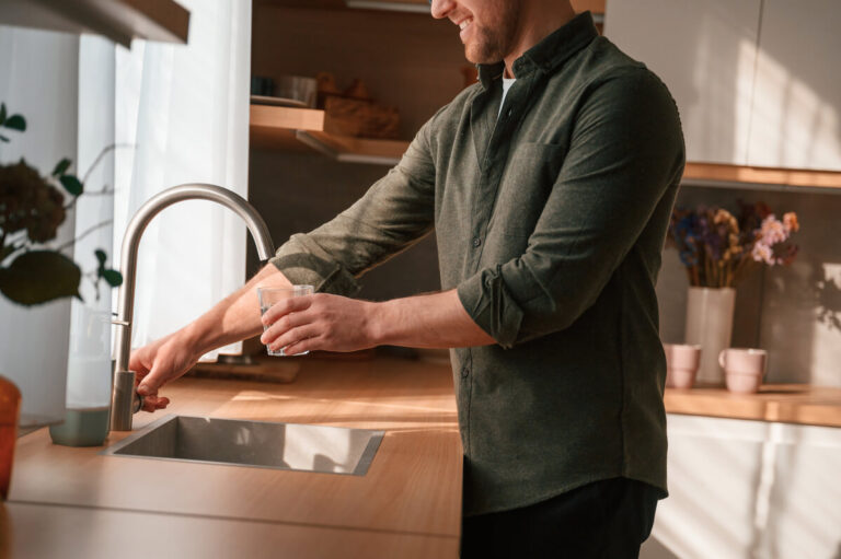 Un particulier remplissant un flacon en verre directement au robinet de sa cuisine pour un test de pureté.