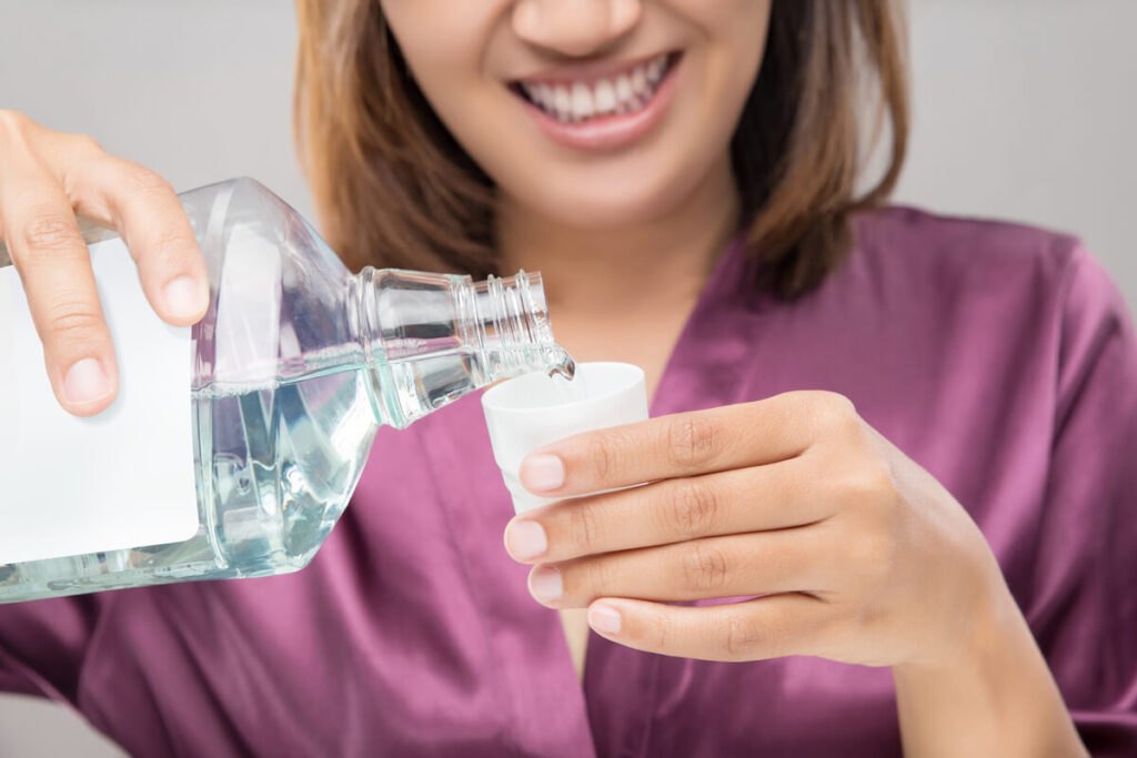 Une personne effectuant un bain de bouche délicat ou appliquant un gel apaisant sur les gencives.