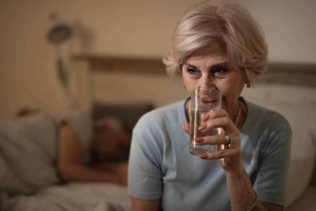 Quels sont les premiers signes de la ménopause à reconnaître ? 2 Une femme d'une cinquantaine d'années buvant un verre d'eau fraîche pour calmer une bouffée de chaleur.