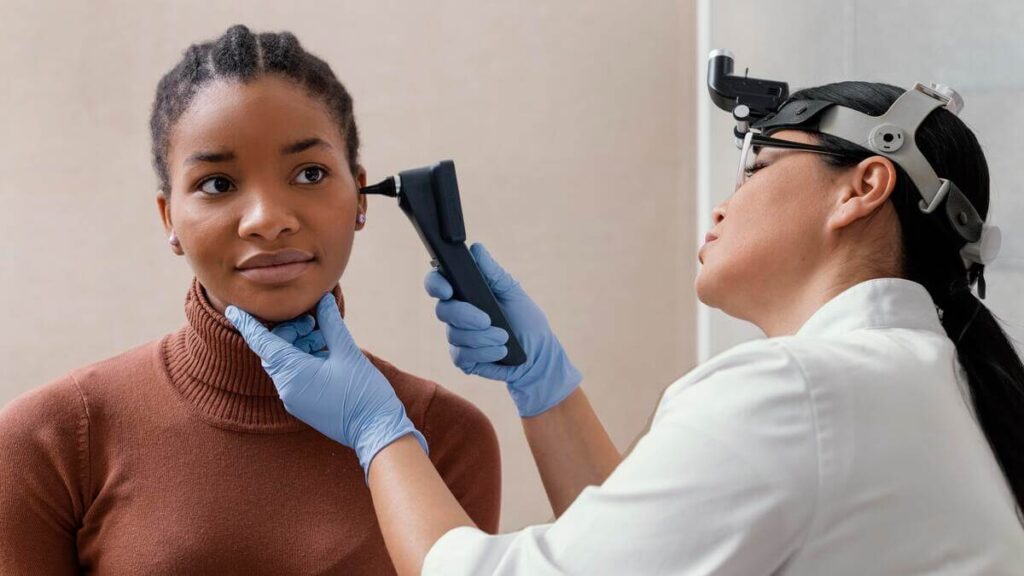 Otite séreuse chez l'adulte et lien avec le cancer : quand faut-il s'inquiéter ? 2 Un médecin ORL examinant le tympan d'un patient adulte à l'aide d'un otoscope en cabinet.