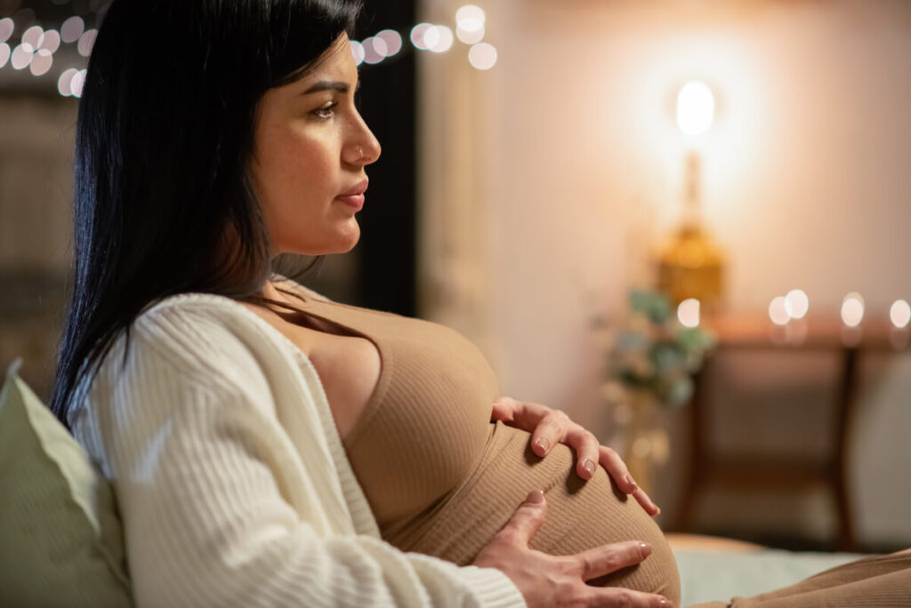 Une future maman pensive touchant son ventre, symbolisant les transformations de la maternité.