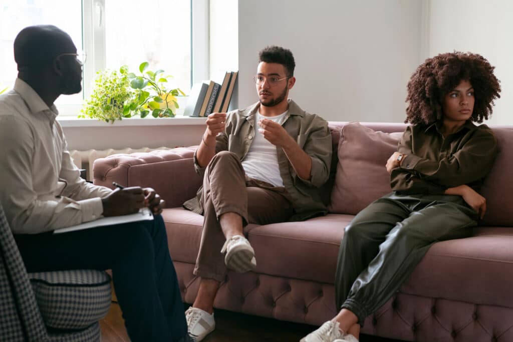 Pourquoi consulter un thérapeute de couple ? 2 Un couple assis sur un canapé discutant calmement avec une thérapeute professionnelle dans un cabinet accueillant.