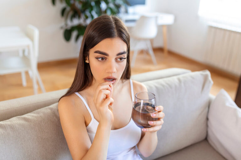 Une femme prenant son comprimé de vitamines prénatales avec un grand verre d'eau le matin.