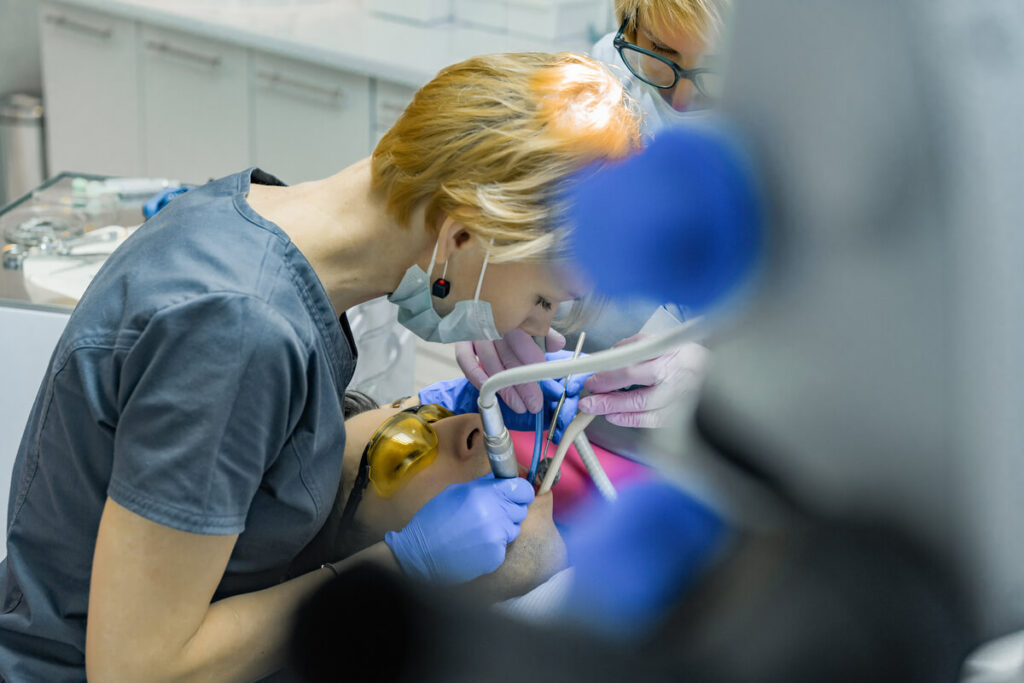 Chirurgienne-dentiste posant une couronne prothétique sur une dent de patient.