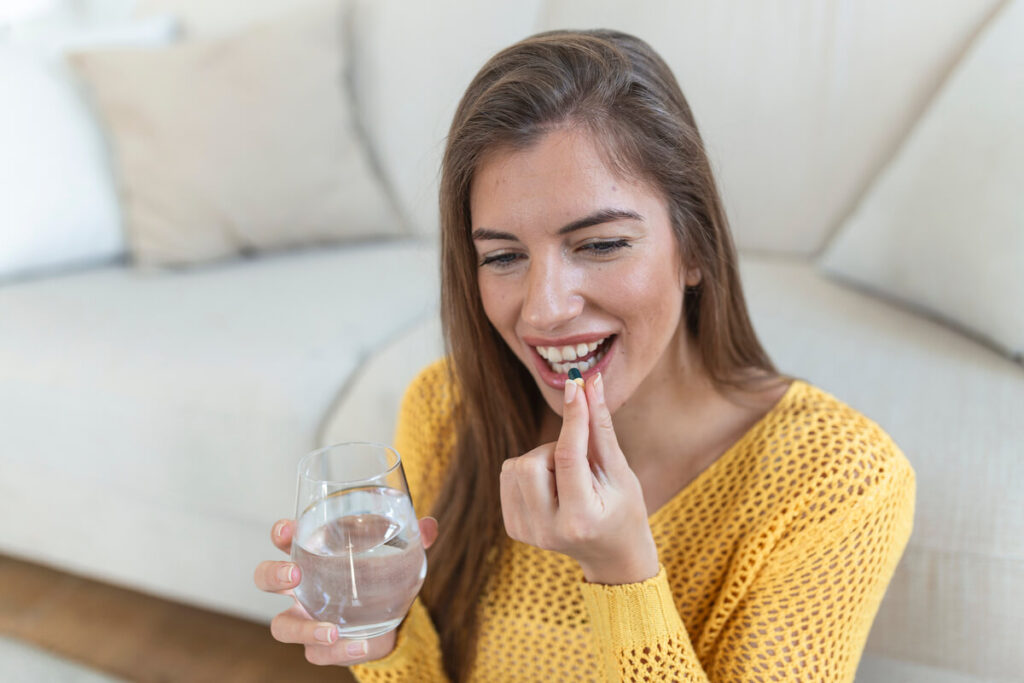 Personne prenant une gélule de complément alimentaire avec un verre d'eau au cours de son déjeuner.