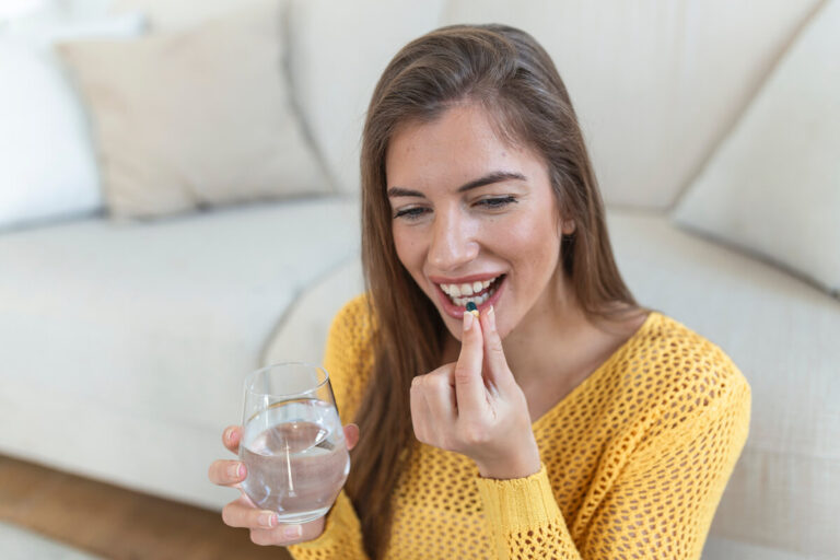 Accueil 1 Personne prenant une gélule de complément alimentaire avec un verre d'eau au cours de son déjeuner.