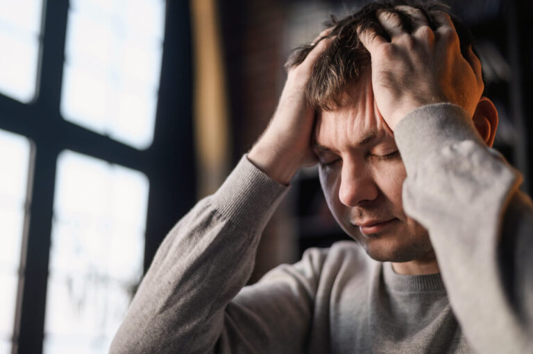 Personne assise se tenant la tête pour faire face à une crise de vertige et à un étourdissement.