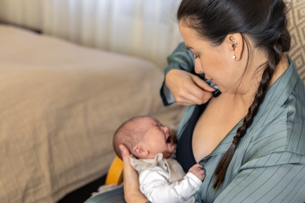 Mère tentant de calmer son nouveau-né qui pleure et se cambre pendant la tétée.