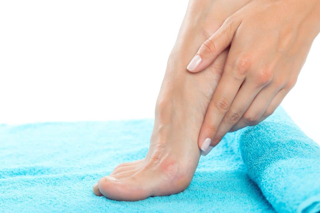 Application d'une crème réparatrice à l'urée sur des talons fendillés.