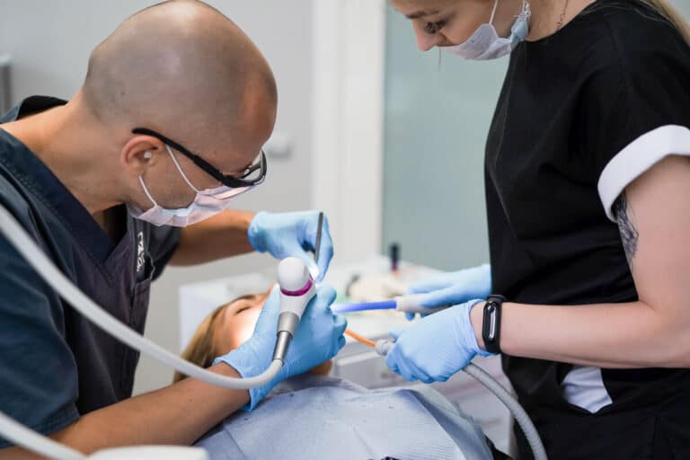 Chirurgien-dentiste réalisant un détartrage ultrasonique pour éliminer le tartre noir au dos des dents du bas.