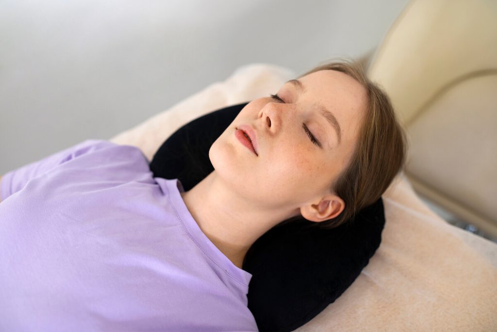 Rhinoplastie : quelles sont les mesures à prendre pour vite récupérer après une chirurgie du nez ? 3 Patiente au repos assise avec des coussins maintenant la tête surélevée pour réduire le gonflement après une rhinoplastie.